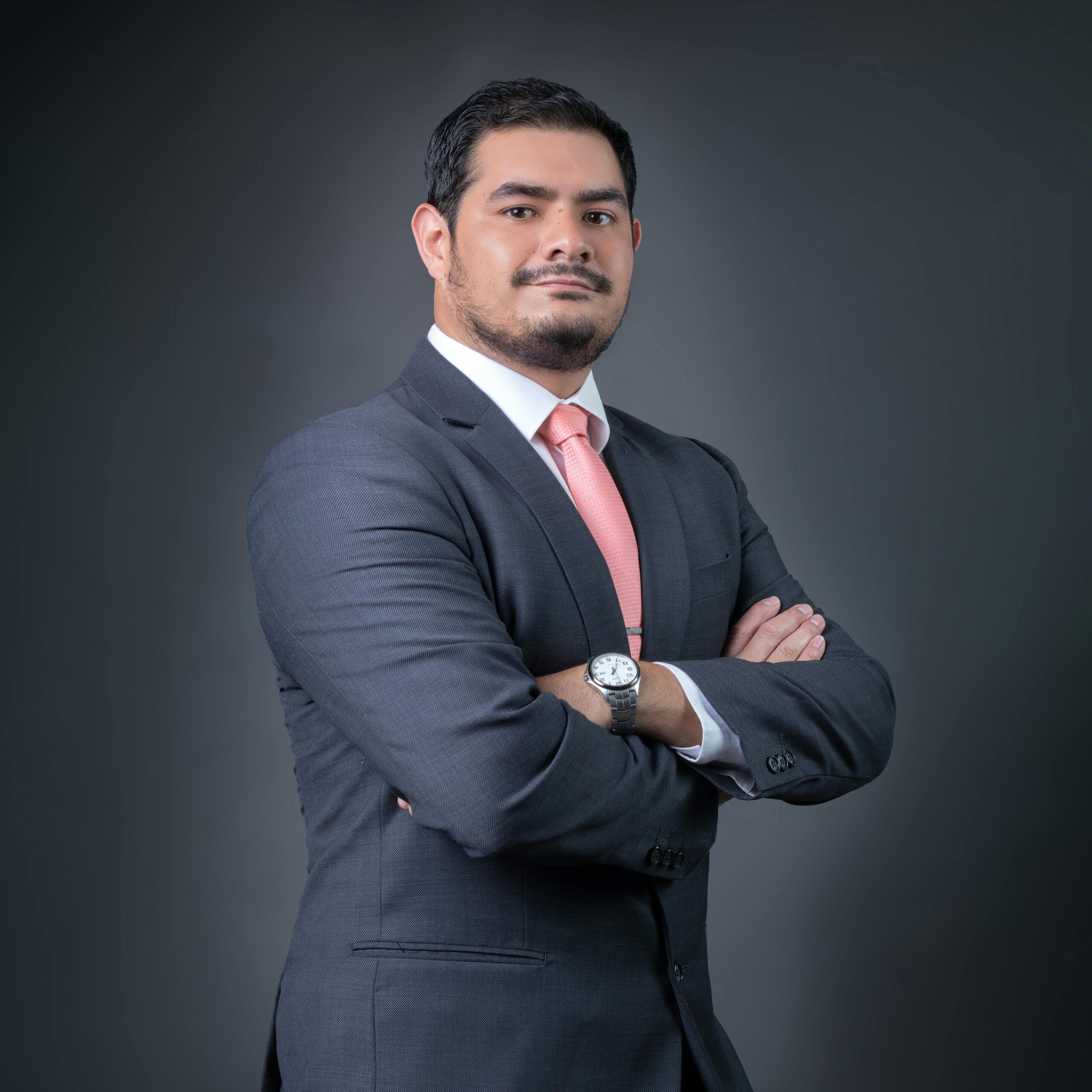Professional portrait of a confident businessman in a gray suit with a pink tie, posing with arms crossed.